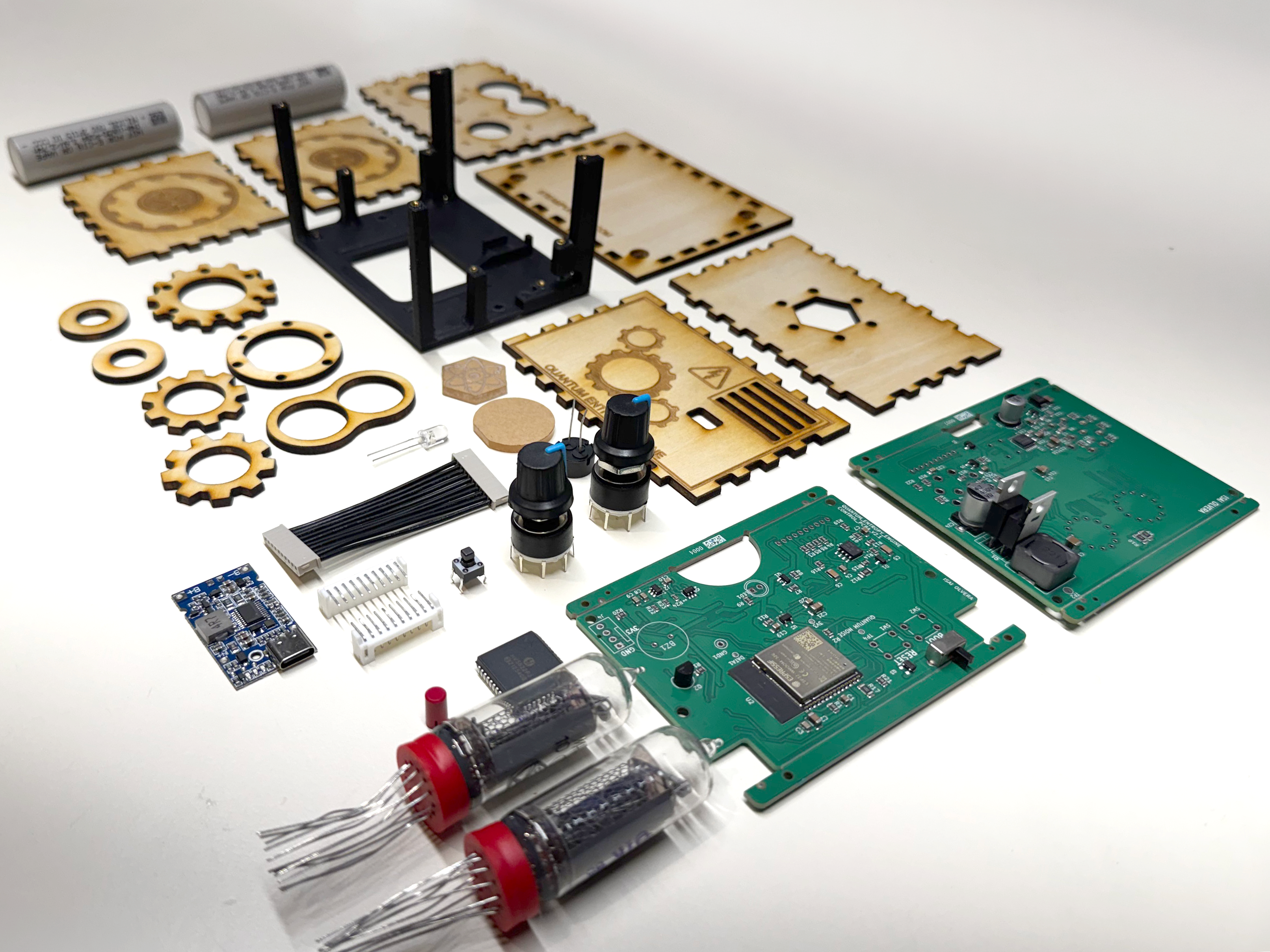 Components of a disassembled quantum entropy engine: expedition kit. The components are all laid out on a white backdrop. The components include the laser cut wooden enclosure, the PCBA holder, PCBAs, ICs and electrical components, and the Nixie tubes. View is isometric.