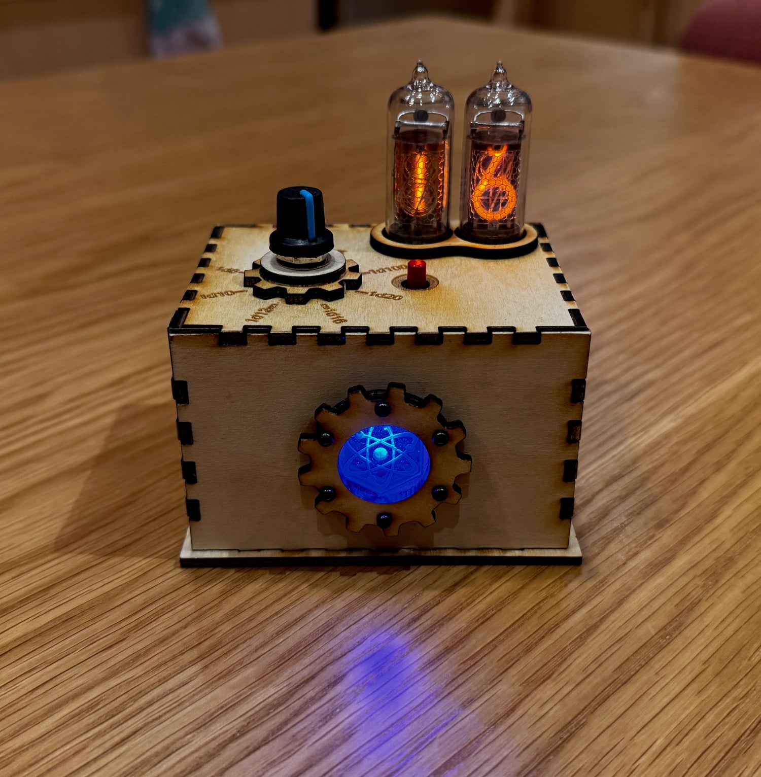 Quantum Entropy Engine: Adventurer in a laser cut wood enclosure with blue LED, displaying 16 on Nixie tubes. Front view. Product sits on a wooden table.
