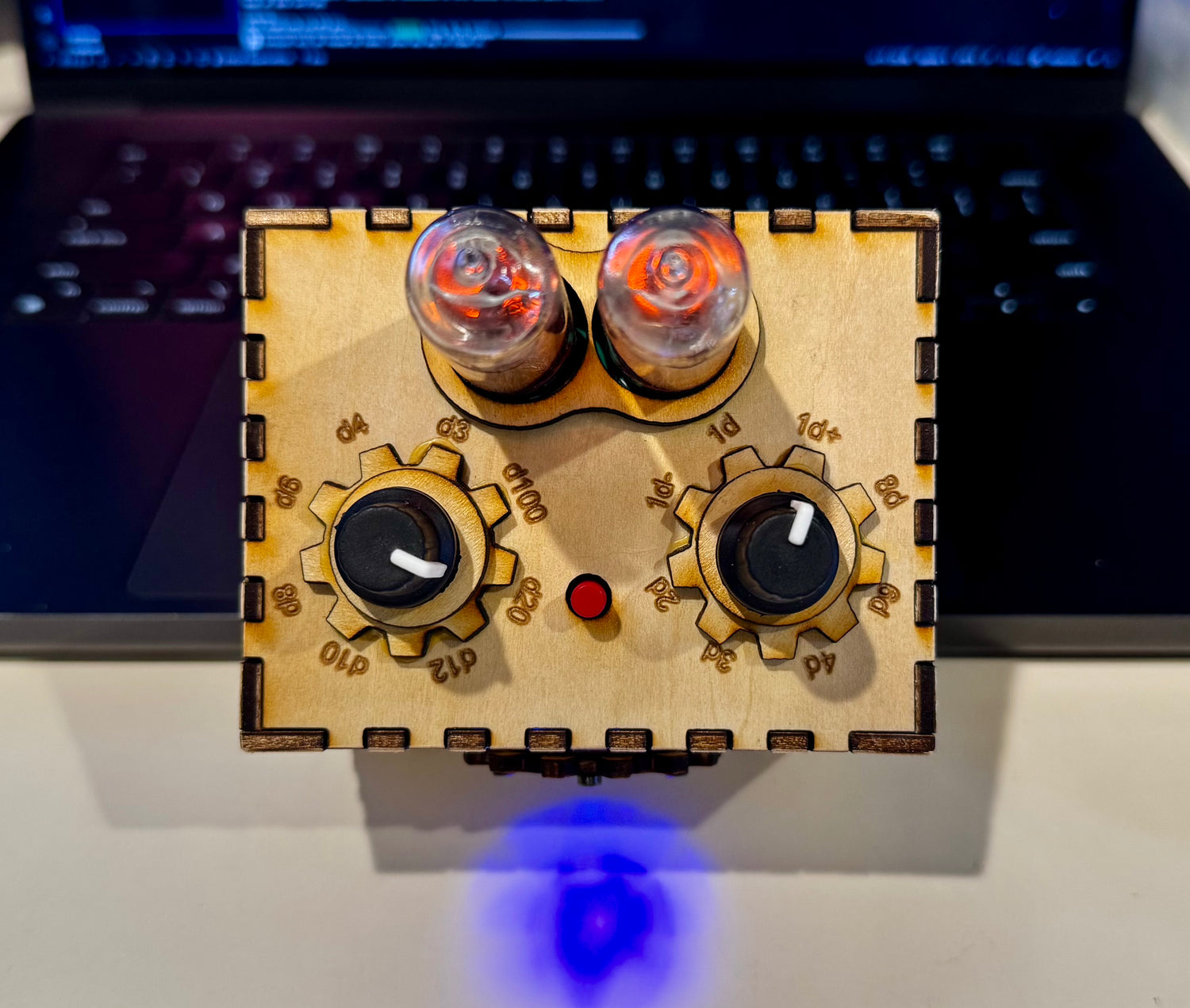 Quantum Entropy Engine: Expedition in a laser cut wooden enclosure. Top down view, showing two dial knobs and the settings the user can select. The quantum entropy engine box sits propped up against a blurred laptop on a lab bench.