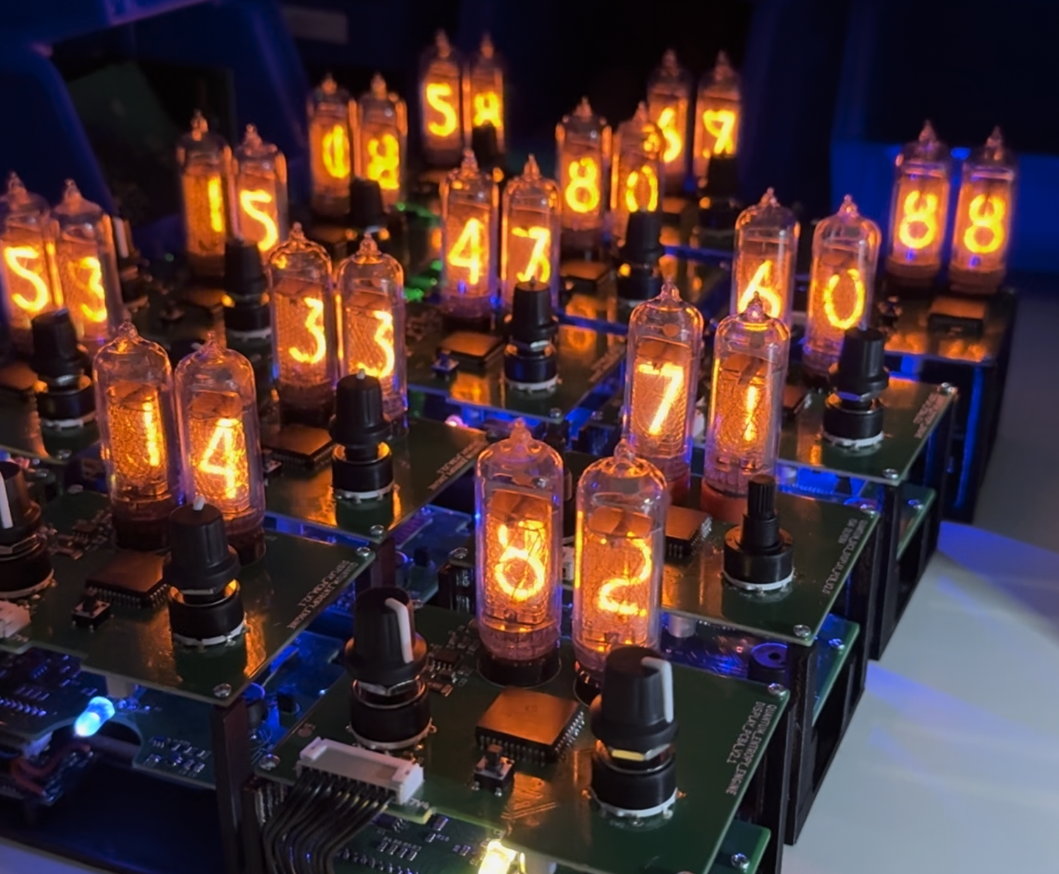 A set of Quantum Entropy Engines sitting in their frames, with circuit boards and components visible. Units do not have an enclosure. All the entropy engines have their Nixie tubes lit up and displaying random numbers between 00 and 99.